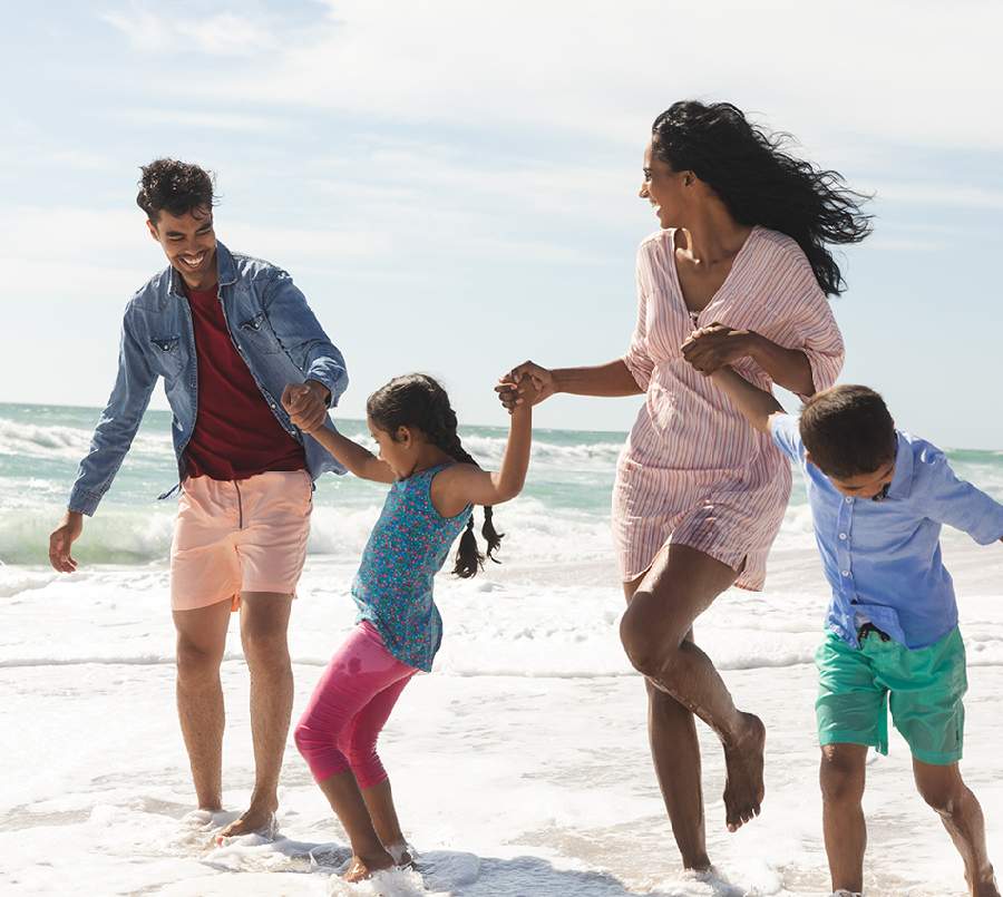 A happy family of four holding hands and running along the shoreline of a beach.