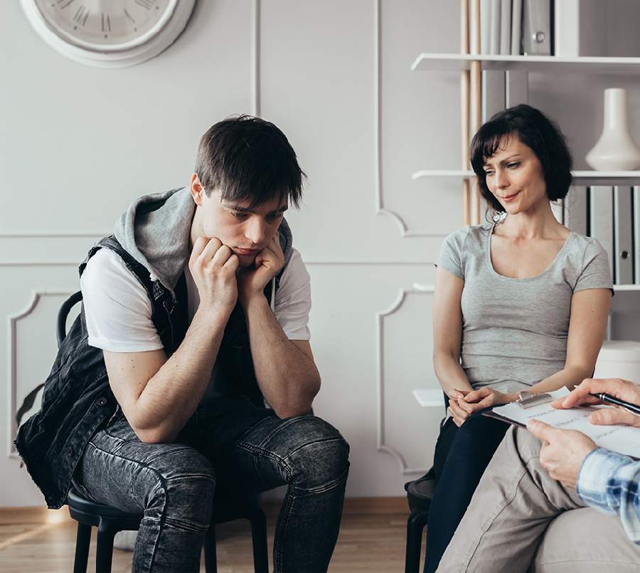 A young man sits with his head down, appearing distressed during a parent coaching session.